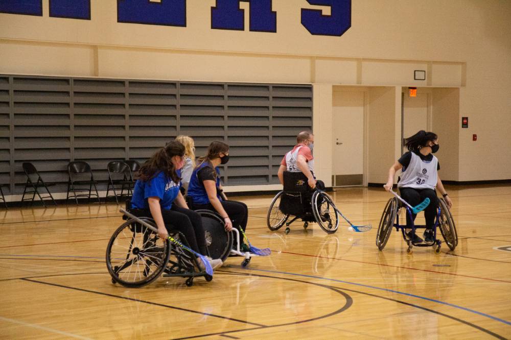 Adults in wheelchairs playing floor hockey.